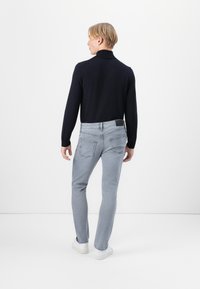 Marineblaues langärmliges Strickpolo-Shirt, kombiniert mit hellgrauen Slim-Fit-Jeans und weißen Sneakers. Einfaches und sauberes Design, minimale Details.