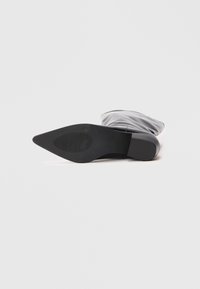 Svart ankelstøvel med spiss tå, glatt syntetisk materiale, flat såle og teksturert grep-mønster på bunnen.