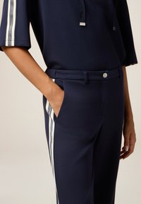Completo blu navy composto da una maglietta ampia e pantaloni a sigaretta con strisce bianche ai lati, dettagli con tasche e chiusura frontale con bottoni. Tessuto dal tocco morbido.