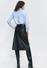 Niebieska i biała koszula w paski z długimi rękawami, zestawiona z czarną skórzaną spódnicą midi oraz błyszczącymi, czarnymi kozakami do kolan.