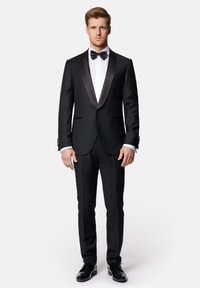 Czarny smoking z satynowym odwróconym kołnierzykiem, biała koszula i czarny muszka. Dopasowany krój, gładka faktura, dopełniony błyszczącymi czarnymi butami.