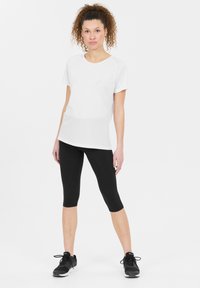 Vitt kortärmat sporttröja i kombination med svarta capri-leggings och svarta träningsskor. Slät textur, avslappnad passform, minimalistisk design.