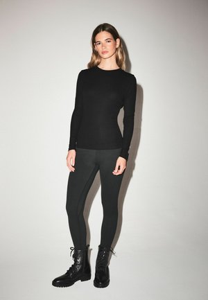 Melna garo piedurkņu blūze kopā ar melniem leggings un melnām šņorējamām kaujas zābakiem. Gluda auduma izskats ar pieguļošu siluetu.