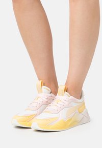 Rosa und gelbe Sneakers mit einem Obermaterial aus Mesh und synthetischem Material, strukturierten Akzenten und einer dicken weißen Sohle, die mit Schnürverschluss und Branding ausgestattet sind.