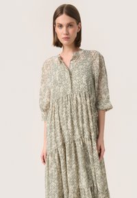 Vestido verde claro de capas en un tejido transparente y texturizado con patrones abstractos y un cuello tipo camisa; mangas tres cuartos.