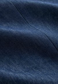 Dunkelblauer Denimstoff mit sichtbarer diagonaler Webstruktur und feiner Nahtlinie, leicht zerknittert und gefaltet.