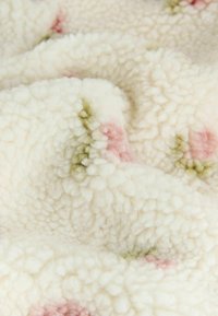 Blødt, hvidt fleece-stof med en struktureret, fluffy overflade. Har spredte lyserøde og grønne prikker over det hele.