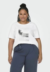 Valkoinen puuvillateeppari, jossa on mustavalkoinen rantakuvasto helmikoristeilla. Rentomallinen, pyöreä kaula-aukko, yhdistetty tummansinisiin housuihin.