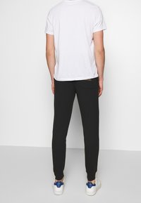 Svarta slim-fit joggers i mjukt tyg, med en bakficka och ribbad mudd, kombinerade med en enkel vit T-shirt och vita sneakers.