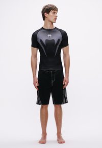 Μαύρο αθλητικό rash guard με γκρι λεπτομέρειες και εφαρμοστή σχεδίαση, συνδυασμένο με μαύρο μαγιό σορτς με λευκές ραφές και κορδόνι στη μέση.