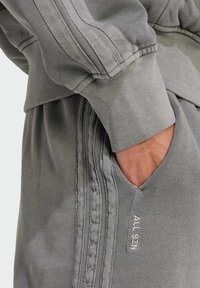 Gray sweatshirt with ribbed cuffs and hem. Features a pocket on the front and vertical stitching along the sides. Embroidered text "ALL SZN."