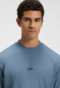 Felpa blu a maniche lunghe con scollatura rotonda e tessuto testurizzato. Presenta un piccolo logo nero "BOSS" sul petto.