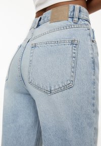 Jeans in denim azzurro chiaro con vita alta, dotati di due tasche posteriori e un'etichetta in pelle marrone chiaro sulla cintura.