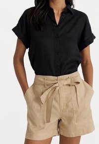 Black short-sleeve button-up shirt paired with beige high-waisted shorts featuring a tie belt and front pockets. Smooth textures and classic design.