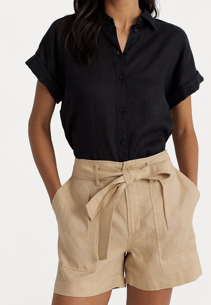 Black short-sleeve button-up shirt paired with beige high-waisted shorts featuring a tie belt and front pockets. Smooth textures and classic design.