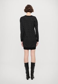 Vestito maglione nero con maniche lunghe, caratterizzato da un motivo a pois, design aderente e polsini a costine. Abbinato a stivali neri al ginocchio.