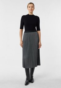 Top corto aderente nero a maniche corte abbinato a una lunga gonna grigia plissettata, caratterizzata da una superficie testurizzata e una vita larga, completata da stivali neri al ginocchio.