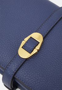 Borsa in pelle grana blu con chiusura a fibbia in metallo dorato con il nome del marchio "Coccinelle" inciso. Cuciture decorative lisce lungo i bordi.