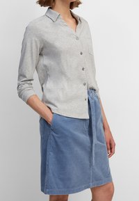 Light gray button-up shirt with long sleeves, paired with a knee-length blue corduroy skirt featuring a tie waist and side pockets.