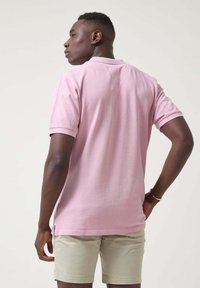 Camisa polo rosa de manga corta, hecha de algodón, con un cuello plano. Combinada con pantalones cortos de color beige claro, mostrando un ajuste relajado.