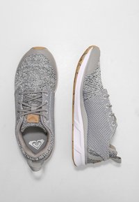 Chaussures de sport grises avec une tige en maille texturée, une semelle rembourrée et une semelle extérieure en caoutchouc naturel contrastant. Caractérisées par un design à lacets et une étiquette de logo.