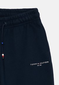 Calças jogger azul-marinho com cintura elástica, cordão e logótipo bordado 'TOMMY HILFIGER' em branco. Textura de tecido de felpa suave.