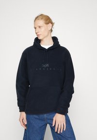 Felpa con cappuccio blu navy in morbido fleece, dotata di tasca frontale, coulisse regolabile e logo stampato. Vestibilità rilassata e maniche lunghe.