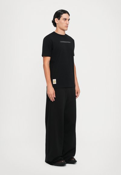 Black short-sleeve t-shirt with a crew neck and subtle logo detail, paired with wide-leg black trousers and black shoes.