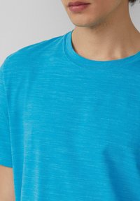 Niebieska koszulka z krótkim rękawem wykonana z lekkiego materiału, z klasycznym okrągłym dekoltem oraz subtelnym wzorem teksturowanym.