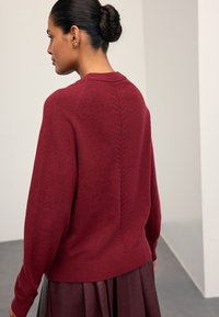 Bordeauxrød strikket sweater med rund halsudskæring, sænkede skuldre og ribbet kant. Har teksturerede detaljer langs bagsømmene.