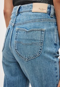 Σιέλ τζιν από τζιν ύφασμα με πίσω τσέπη σε σχήμα καρδιάς, ψηλό ζωνάκι και μπεζ ετικέτα στο πίσω μέρος με την επιγραφή «Pepe Jeans London».