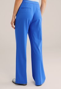 Nohavice so širokými nohavicami v žiarivej modrej farbe. Vyrobené z hladkej látky, s dvoma zadnými vreckami a voľným strihom. Kombinované so svetlými topánkami.