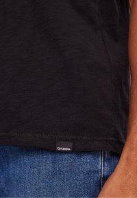 Svart kortärmad skjorta i ett lätt, strukturerat tyg. Har en GABBA-etikett vid fållen. Bärs med blå denimjeans.