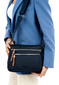 Borsa a tracolla navy realizzata in tessuto con due zip frontali e dettagli in pelle marrone. Presenta una tracolla regolabile e una texture liscia.