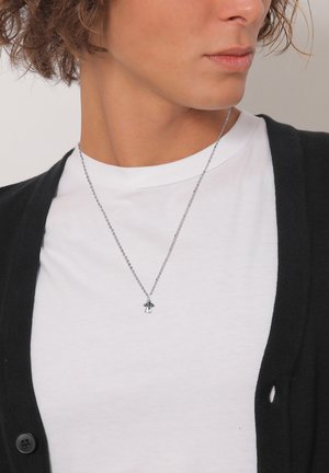 Silver chain necklace with a small pendant featuring a black and white design, worn over a white t-shirt and black cardigan.