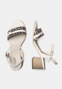 Sandali con stampa leopardata, con cinturini in pelle bianca, tacco basso e hardware decorativo. Texture morbida e palette di colori neutri.