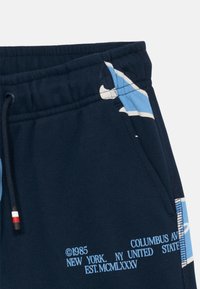 Marinen blå shorts med elastisk midjebånd, snor med rød, hvit og svart tupp, lomme, lys blå grafikk og hvit tekst som leser "1985 Columbus Ave, New York, NY."