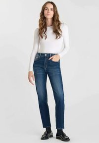 Blå denimjeans med hög midja, rak ben design, femficksmodell och en lätt blekning. Kombinerade med en vit långärmad tröja.