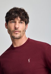 Bordeaux rondehals t-shirt gemaakt van katoen, met een klein wit golferlogo op de borst, een zachte textuur en een klassieke pasvorm.