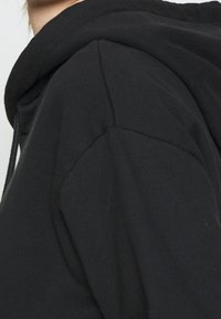 Primo piano di una persona che indossa un hoodie nero, con attenzione alla spalla e a parte dell'area del collo.