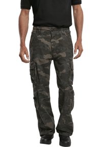 Pantalones cargo en un patrón de camuflaje gris oscuro, fabricados con un tejido duradero, que cuentan con múltiples bolsillos y un ajuste relajado. Se llevan botas negras.