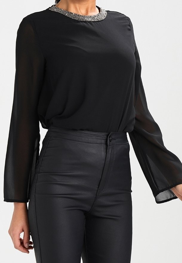 Czarna bluzka z długim rękawem z teksturowanym, ozdobnym kołnierzem, zestawiona z czarnymi skórzanymi spodniami o wysokim stanie. Przezroczysty materiał, gładka tekstura.