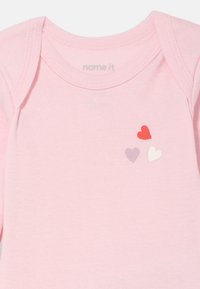 Lys rosa bomullsbody med korte ermer med tre hjerteapplikasjoner i rødt, hvitt og lilla. Myk tekstur og buet halslinning.