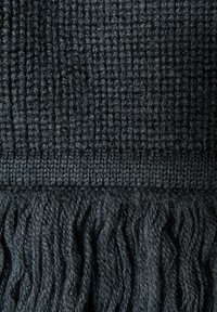 Tissu tricoté sombre présentant un design texturé et côtelé avec un bord à franges. La couleur est un gris anthracite profond avec une épaisseur de fil variable.
