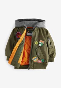 Veste bomber vert olive avec une capuche grise. Doublée en orange, elle comporte plusieurs patchs colorés et une poche zippée sur la manche.