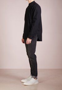Czarna koszula z długim rękawem z wysokim dekoltem, zapinana na guziki, z lekkim ogonem, w połączeniu z ciemnymi dżinsami i białymi sneakersami. Gładka struktura materiału.