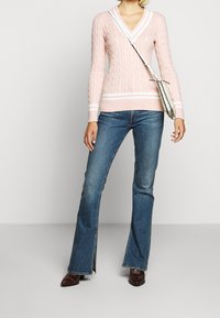 Vaaleanpunainen kaapelikuvioinen neulepaita, jossa syvä V-pääntie ja valkoiset raidat, yhdistettynä sinisiin liehuviin farkkuihin ja tummanruskeisiin kenkiin.