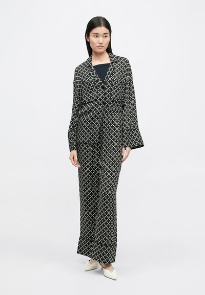 Μαύρο και λευκό κοστούμι με μοτίβο, που διαθέτει μακρύ, ανοιχτό σακάκι με φαρδιές μανσέτες και αντίστοιχα φουστάνια. Λείος ύφασμα με γεωμετρικό σχέδιο.