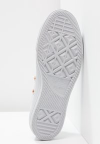 Suola di sneaker in gomma bianca con un distintivo motivo a treccia geometrica, dotata di occhielli in rosa oro e accenti testurizzati lungo il perimetro.