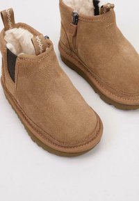 Botas de tobillo de ante marrón con un suave forro de piel de borrego, que cuentan con una cremallera lateral y una suela de goma resistente. Ofrecen una forma de punta redondeada.